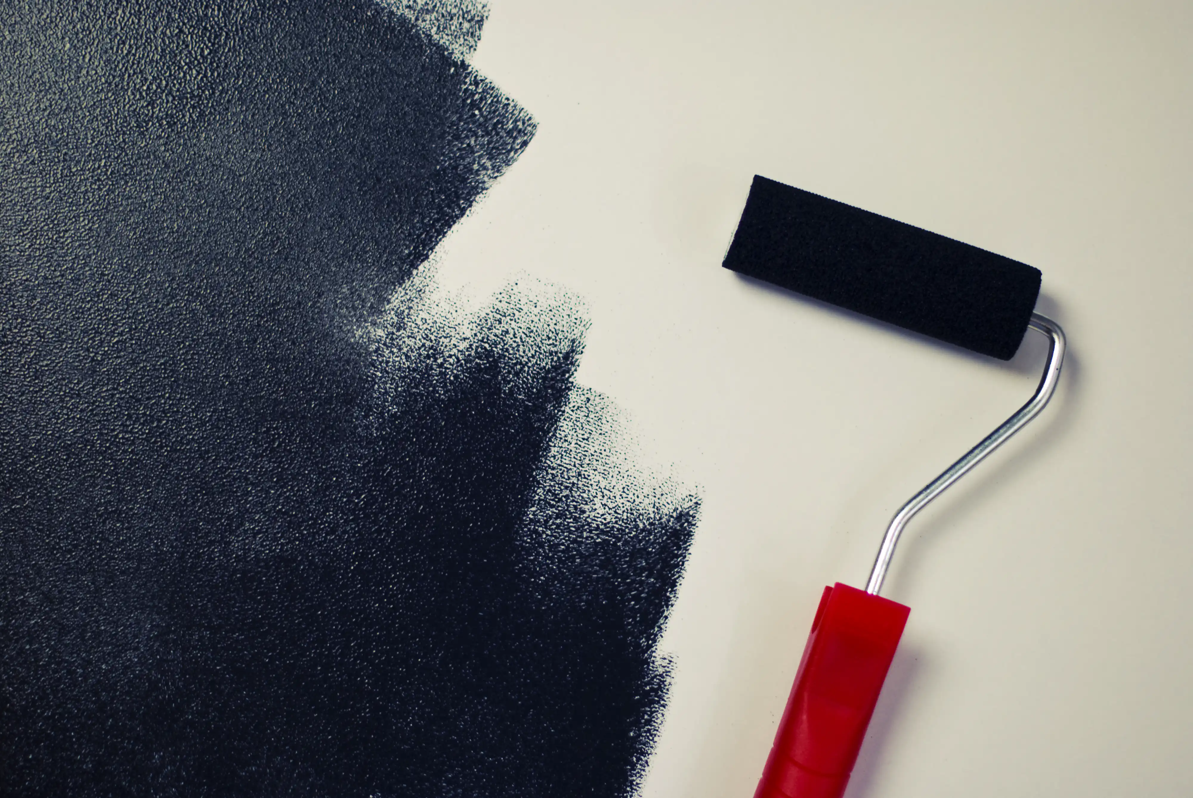 Close-up of a dark textured paint being applied on a white surface with a red-handled roller