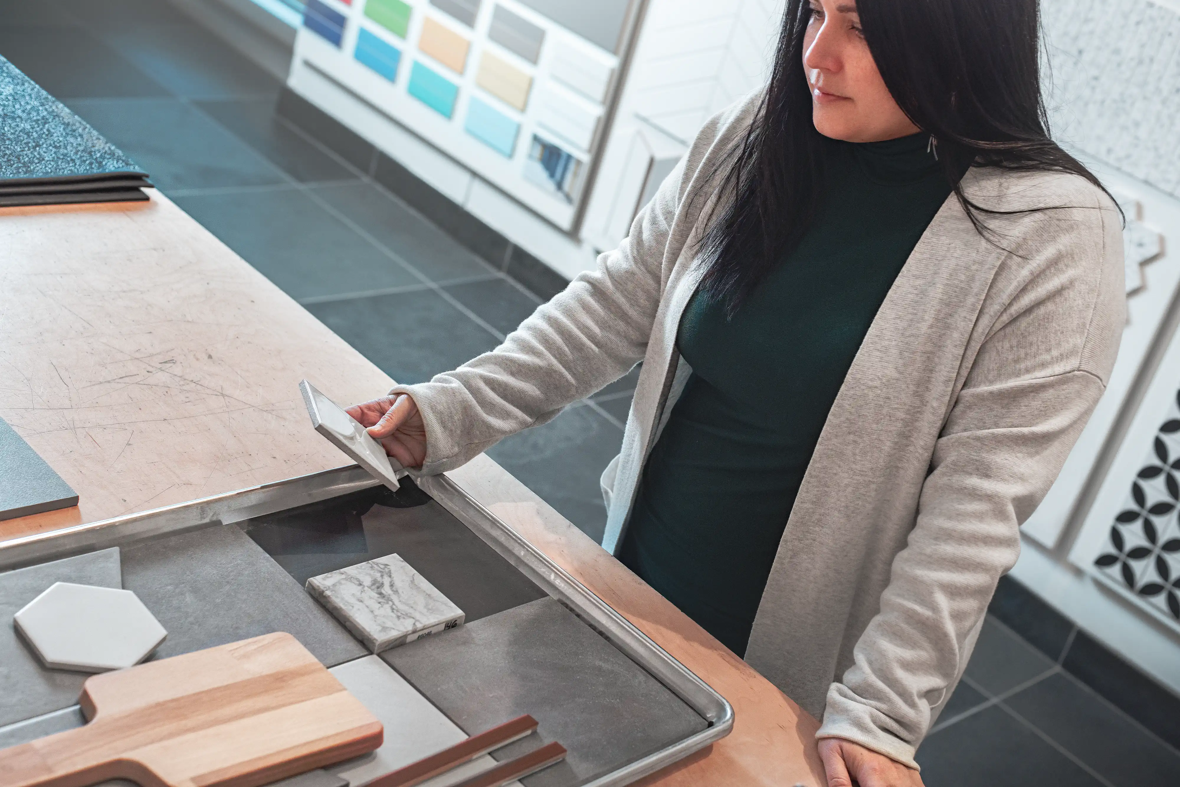 Sarah Brown, designer d'intérieur, compare soigneusement différents modèles de carreaux sur un plateau métallique dans un showroom de décoration de maison chic