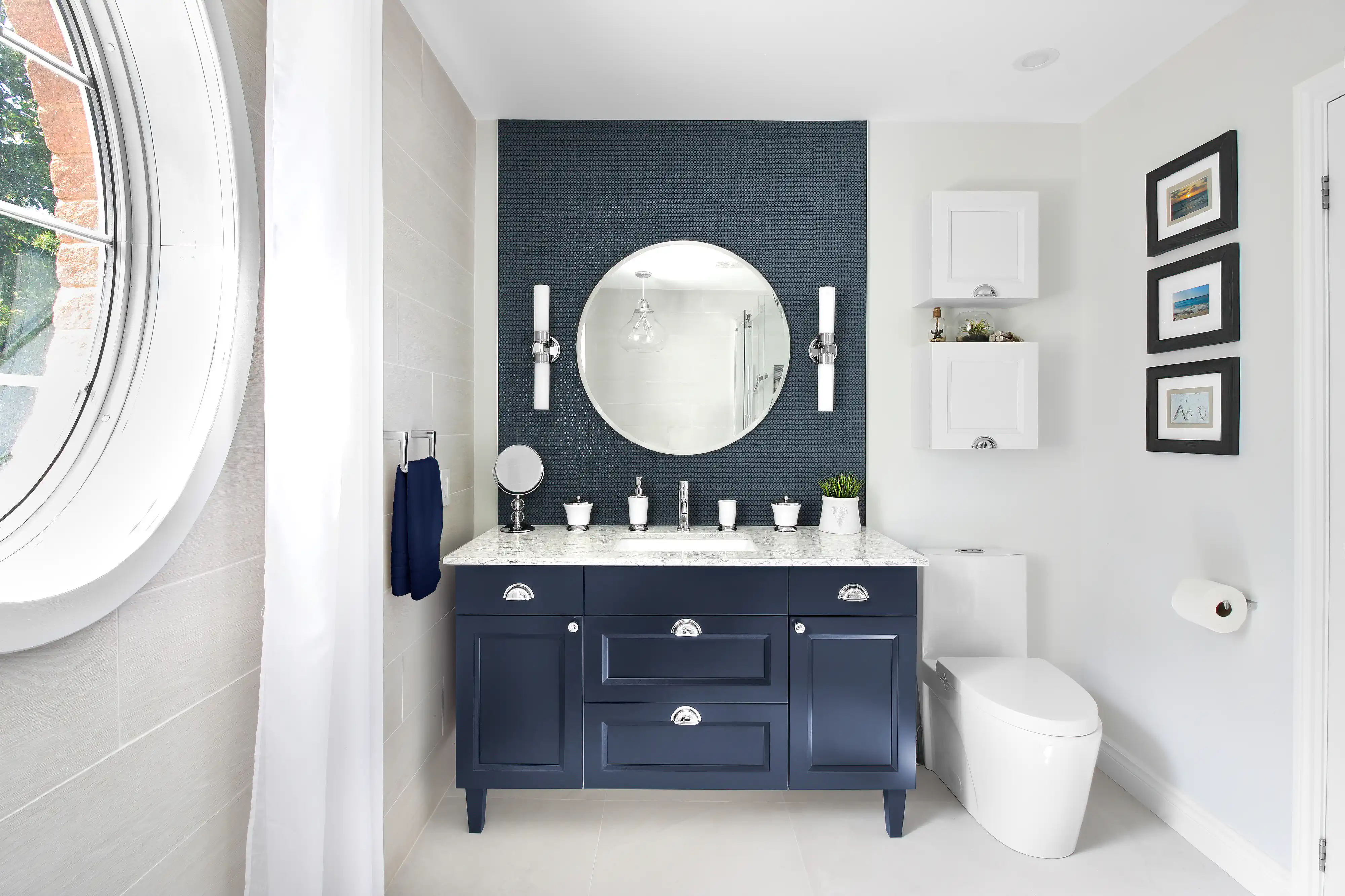 Une salle de bain bleue et blanche avec un miroir rond et un meuble-lavabo, intérieur signé Sarah Brown Design