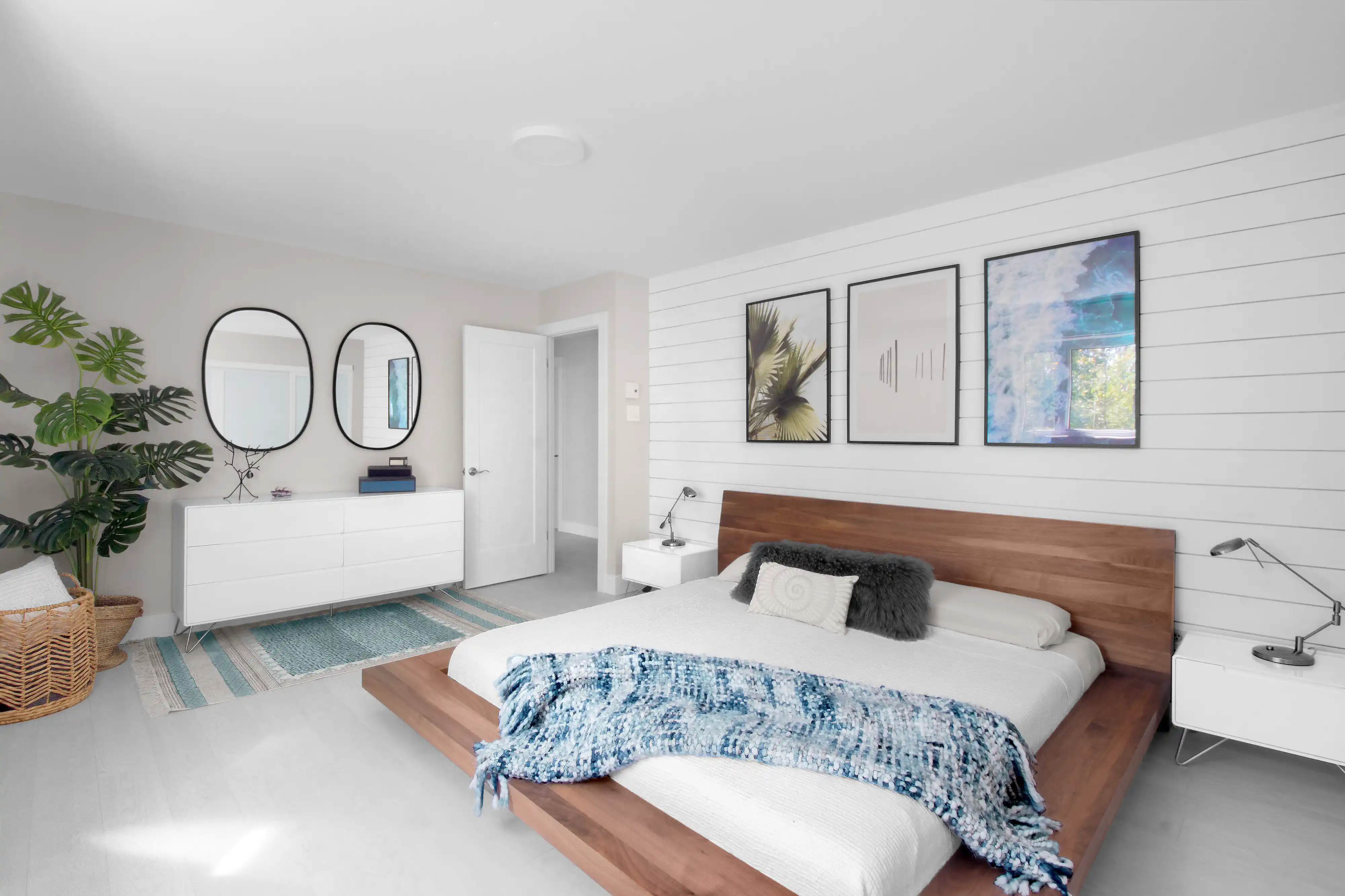 Chambre moderne avec un thème blanc et bois, comprenant un lit en plateforme en bois, une couverture jetée bleue, des tables de nuit blanches et des œuvres d'art encadrées, intérieur signé Sarah Brown Design