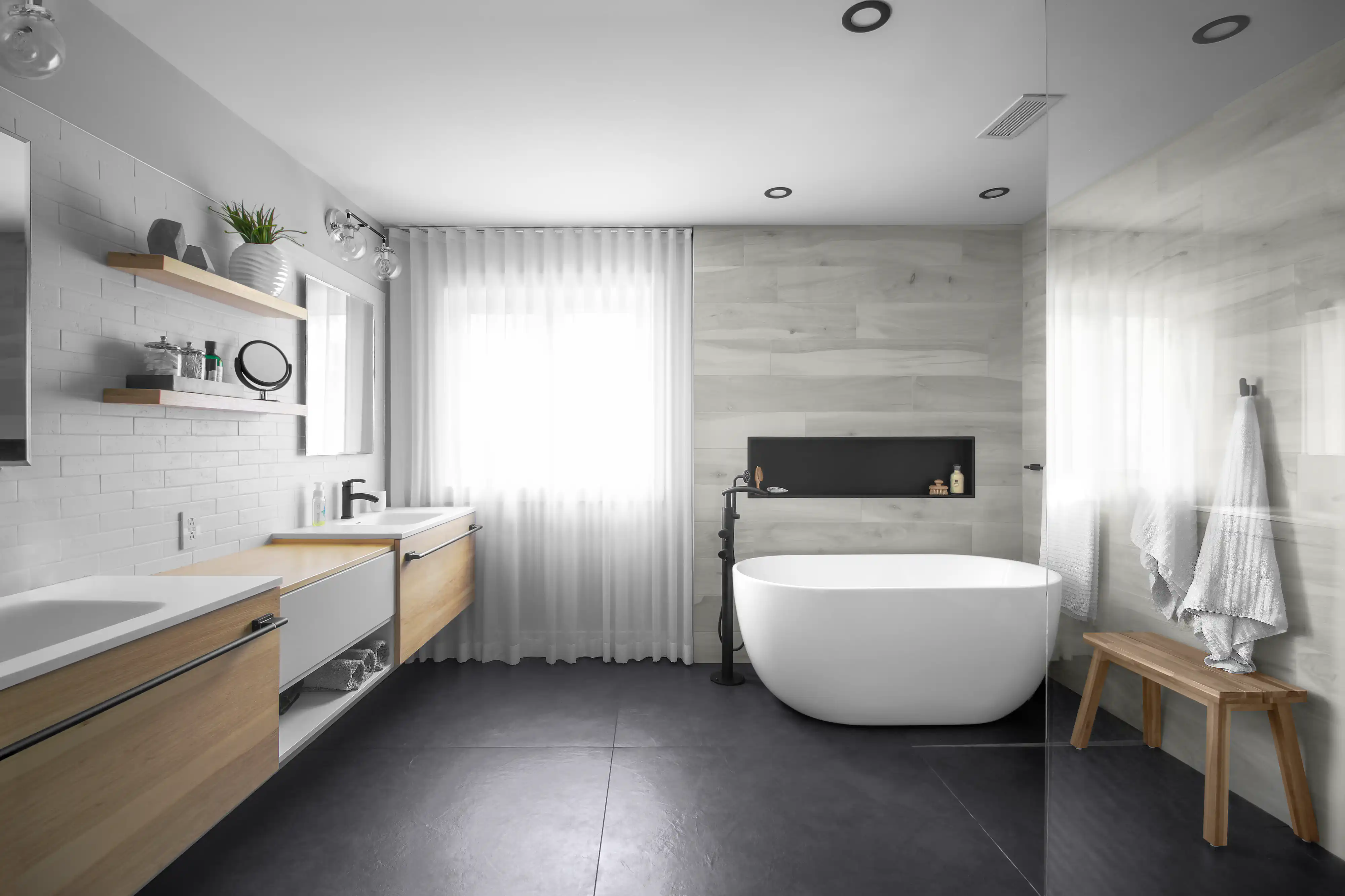 Salle de bain moderne avec une baignoire autoportante blanche, un lavabo sur comptoir en bois et une douche vitrée avec des carreaux noirs, intérieur signé Sarah Brown Design