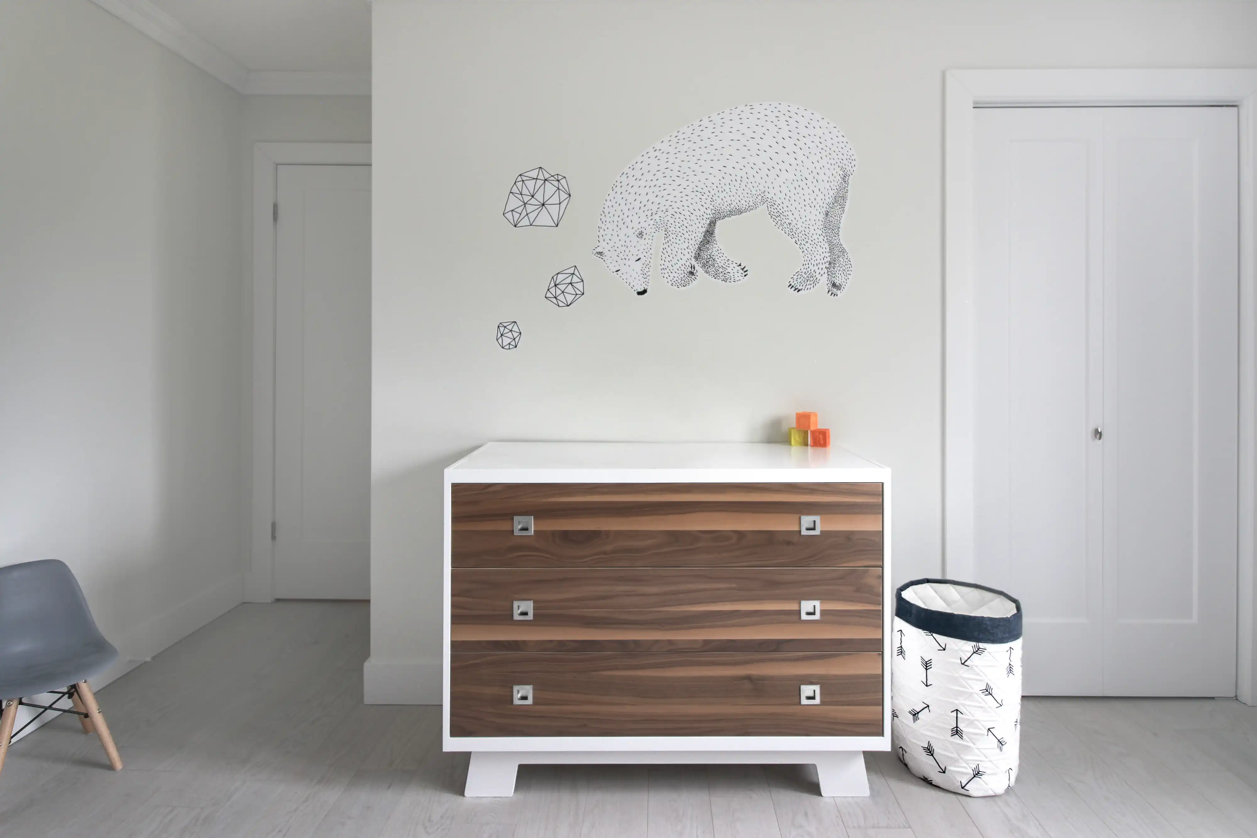 Modern bedroom with a wooden dresser, a blue chair, and a wall with a black geometric bear design, interior by Sarah Brown Design
