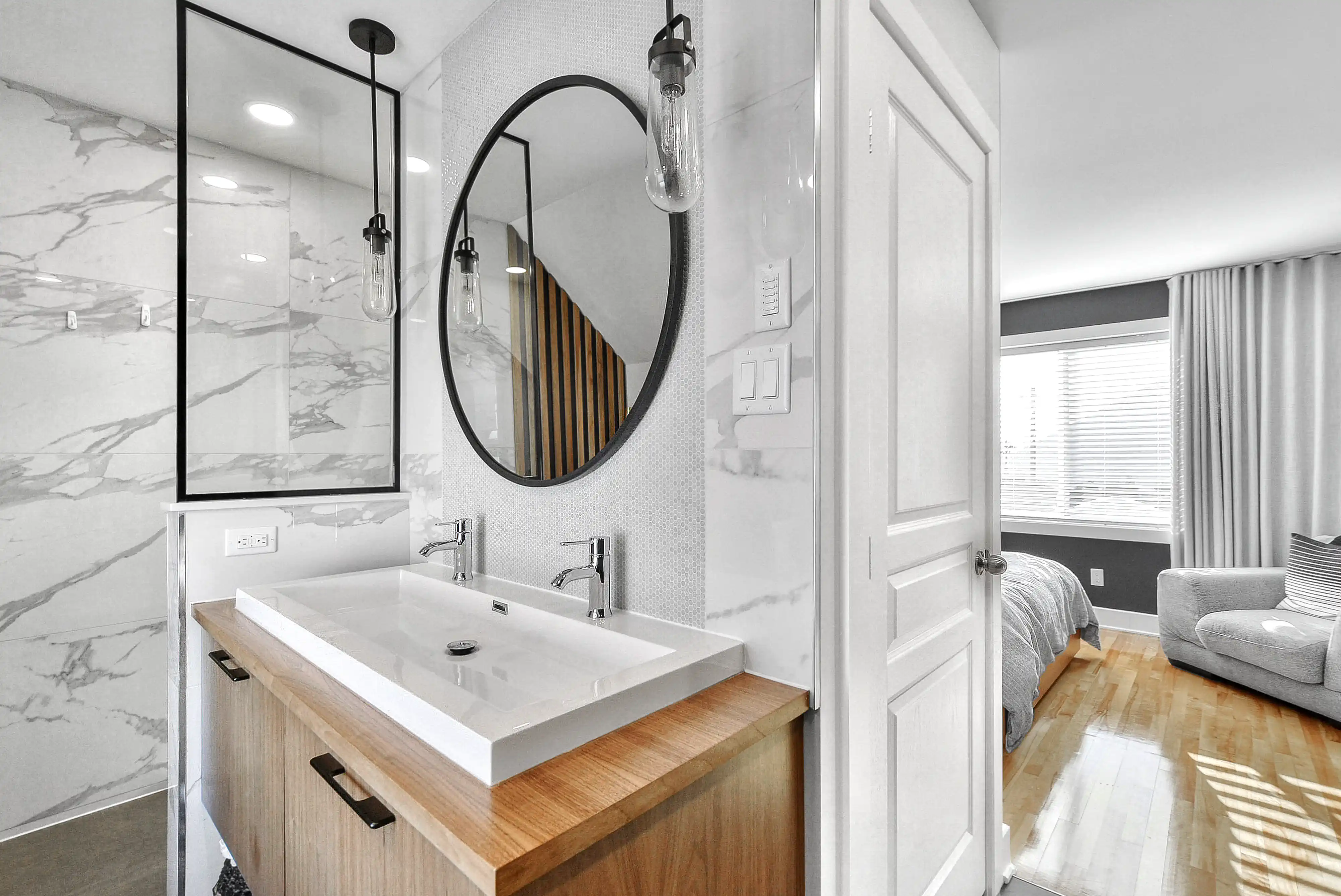 Salle de bain moderne avec un lavabo blanc, un miroir rond avec cadre noir et une douche avec porte en verre, intérieur signé Sarah Brown Design