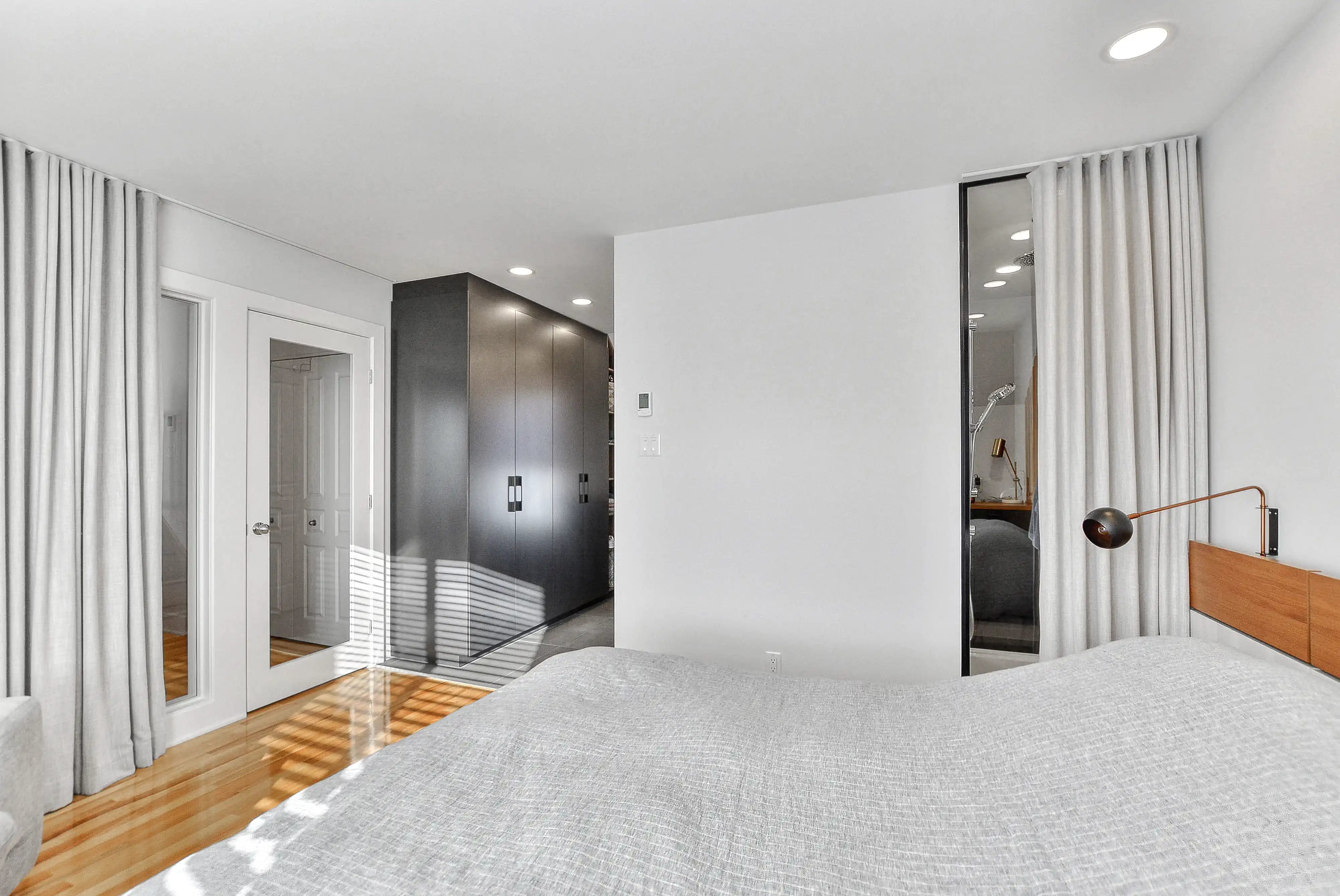 Chambre moderne avec un grand lit, un sol en bois dur et une porte menant à une salle de bain, intérieur signé Sarah Brown Design