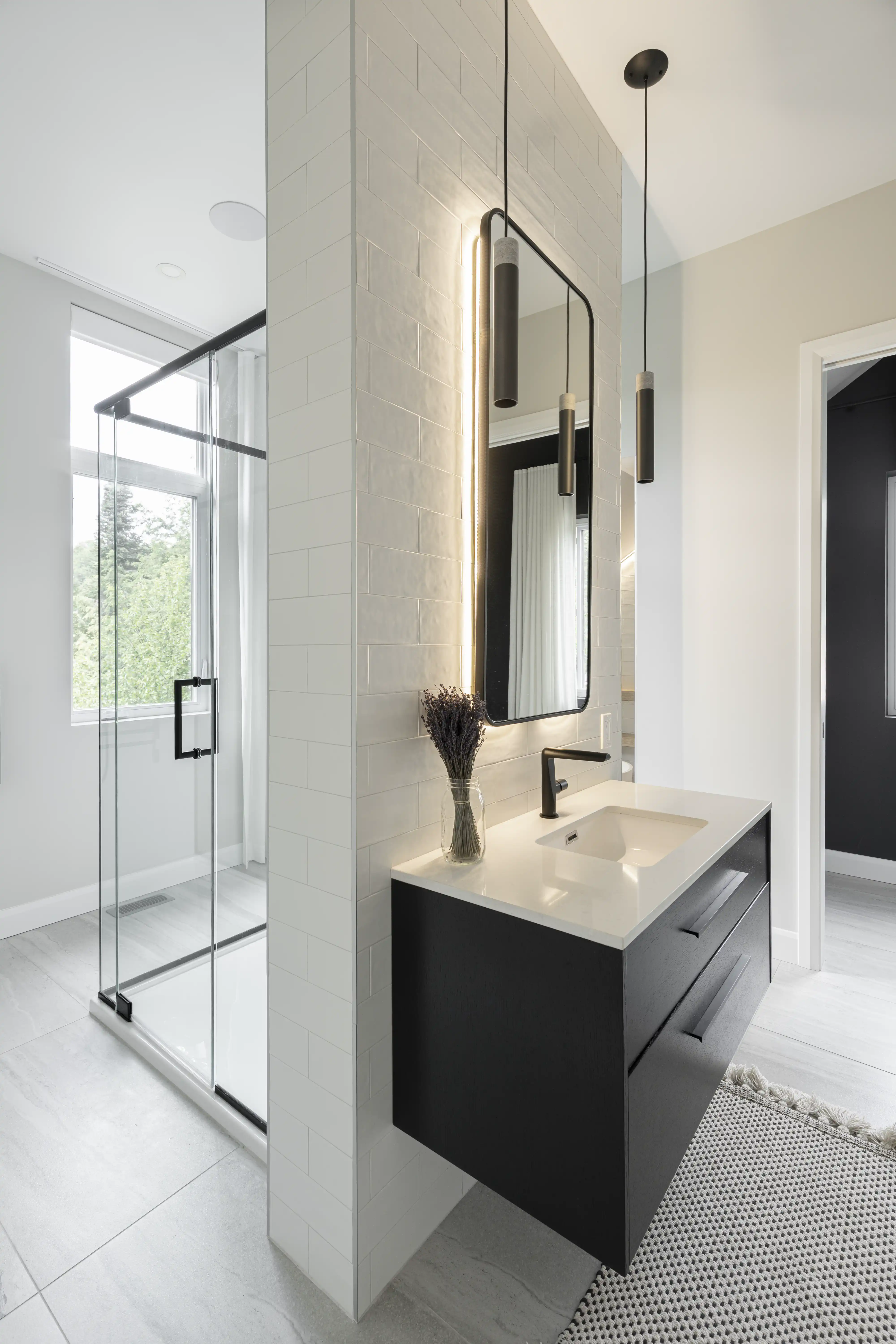 A black and white bathroom with a glass shower enclosure and a window with a view, interior by Sarah Brown Design