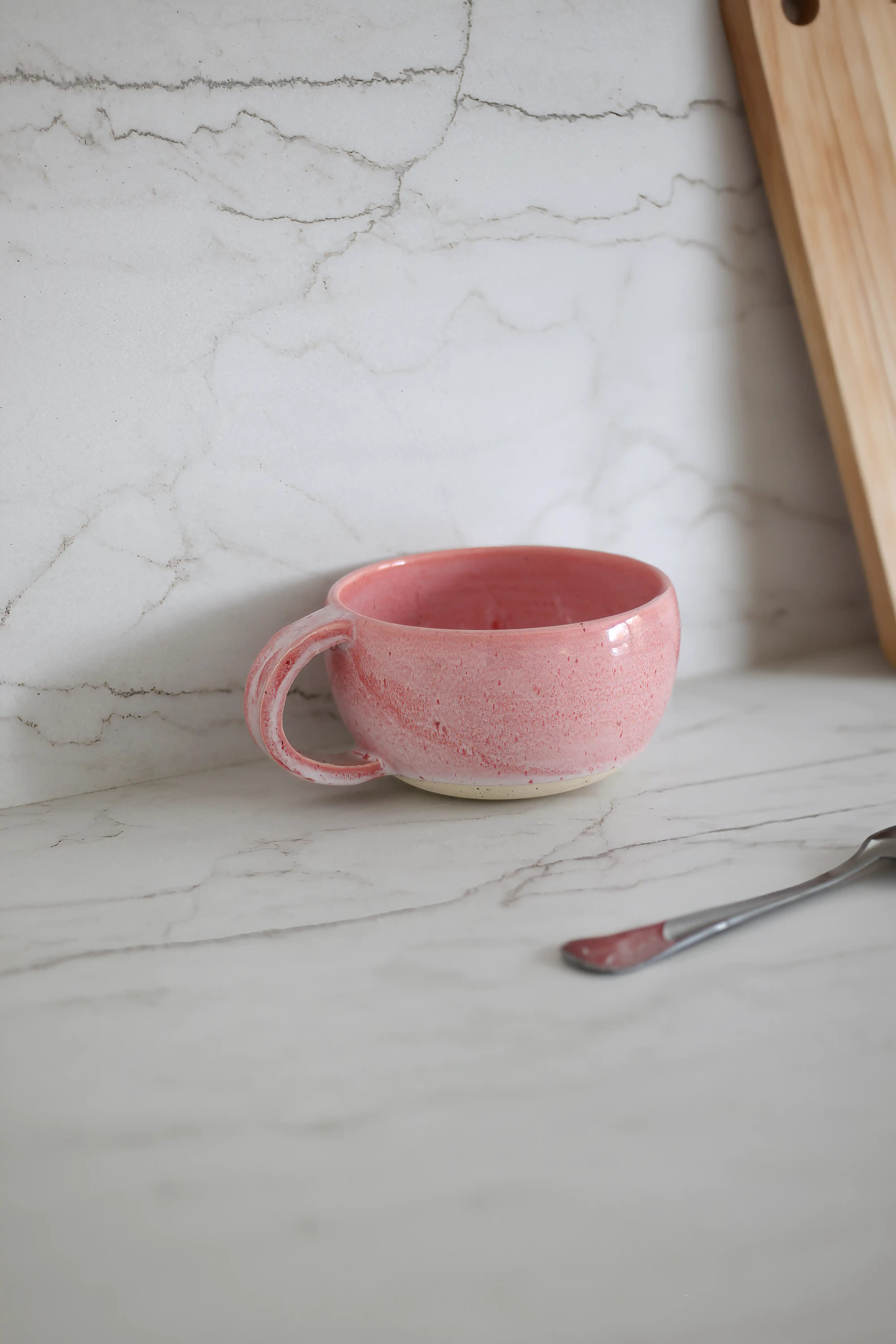 Tasse en céramique rose sur un plan de travail en Dekton blanc aux veines grises subtiles, à côté d'une planche à découper en bois et d'une cuillère en argent, intérieur signé Sarah Brown Design