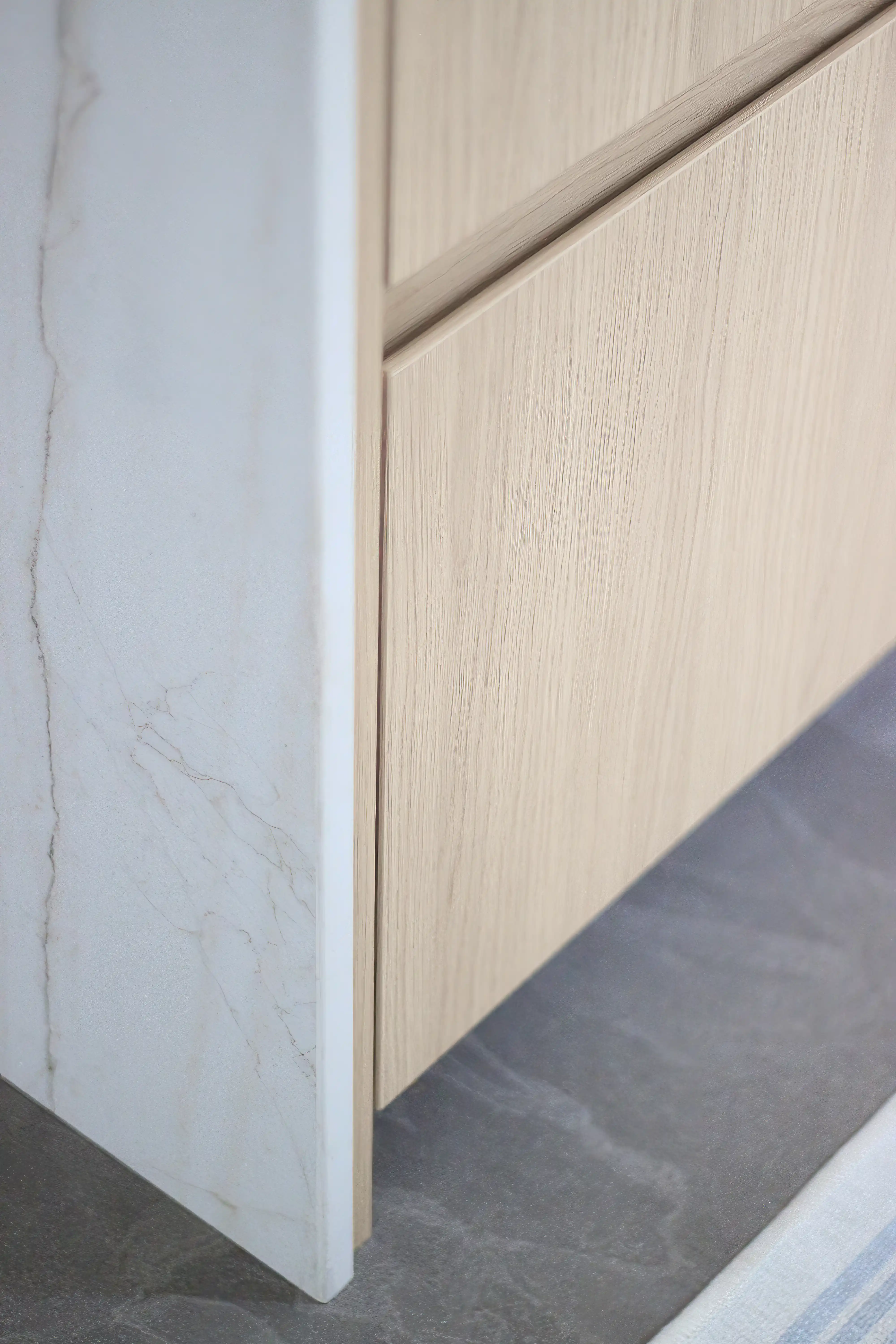 Close-up of a modern interior design featuring a Dekton edge, light wood cabinet, and matte gray flooring, interior by Sarah Brown Design