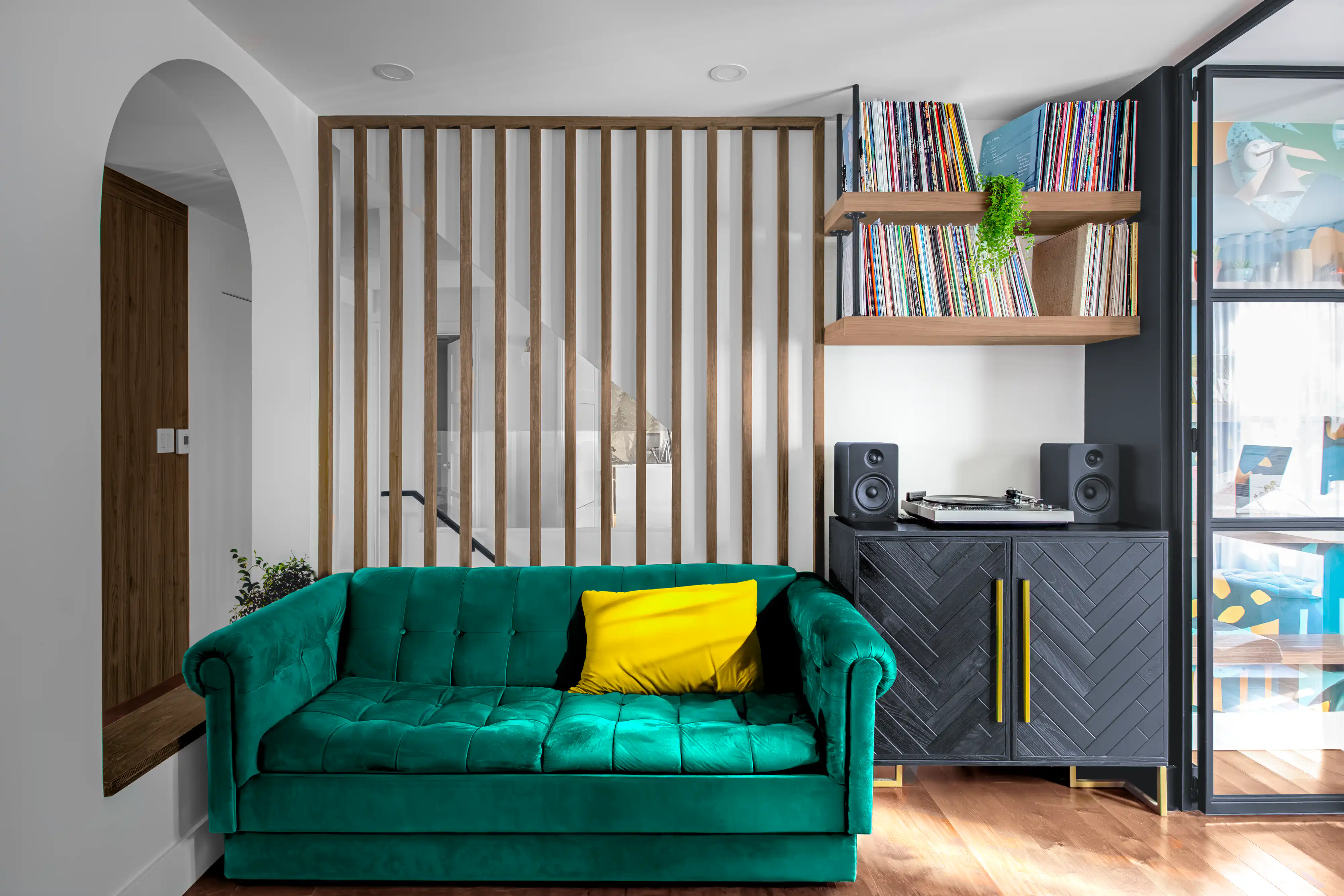 Salon contemporain avec un canapé en velours vert, un séparateur en bois et un coussin jaune vif, intérieur signé Sarah Brown Design