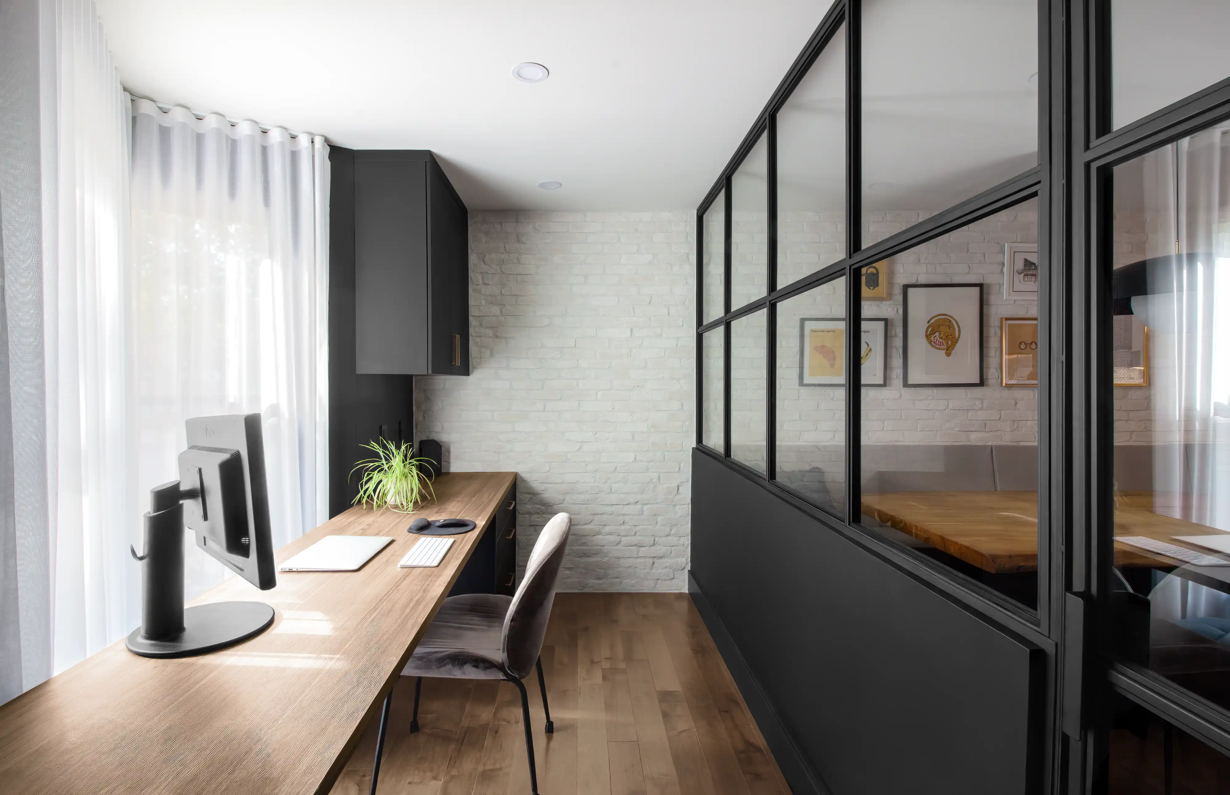 Bureau à domicile épuré avec un long bureau en bois, une chaise moderne et une cloison avec des panneaux de verre, intérieur signé Sarah Brown Design