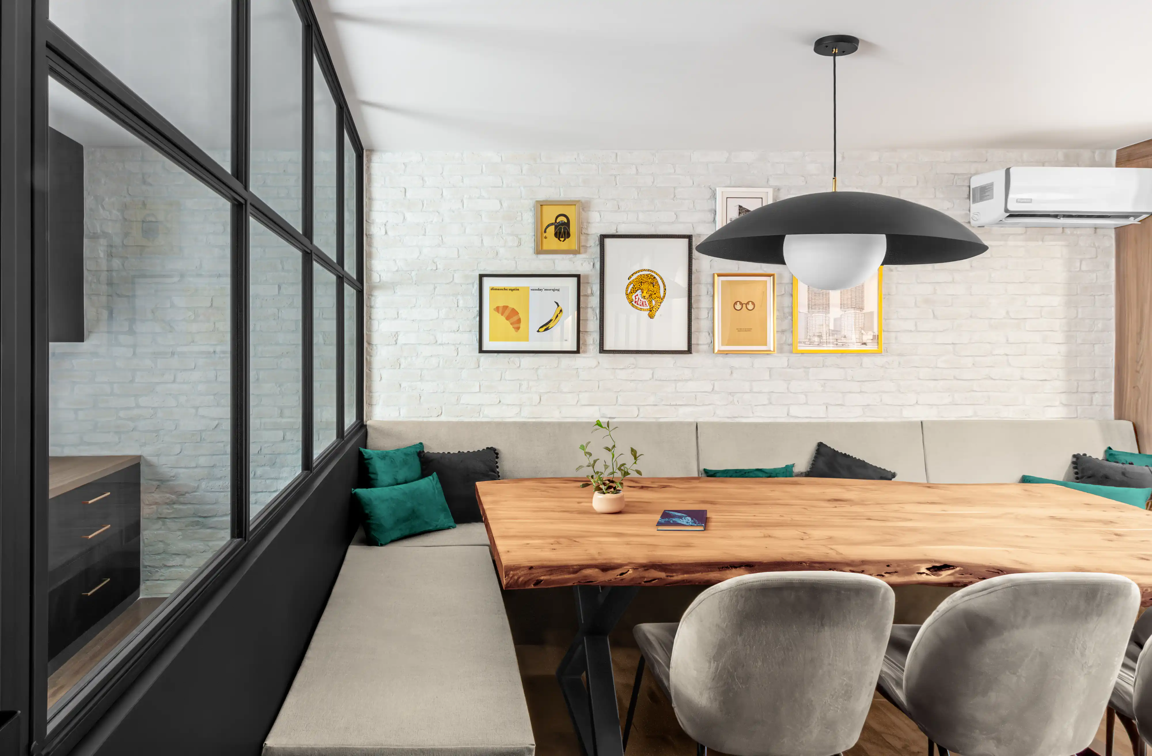 Salle à manger minimaliste avec un mur en briques apparentes, de l'art moderne et une table en bois avec des sièges variés, intérieur signé Sarah Brown Design